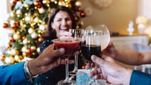 Group of people raising wine glasses in front of a beautifully decorated Christmas tree.