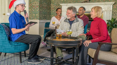 People gathered around a table with a man wearing a Santa hat doing a quiz.