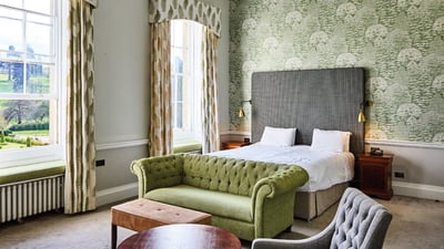 Experience comfort and tranquility in a Warner hotel room with stylish green furniture and a window offering scenic views.