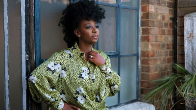 YolanDa Brown standing against a wall with blue window